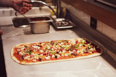 Pizza şefi ticari bir mutfakta sosu tabana koydu.