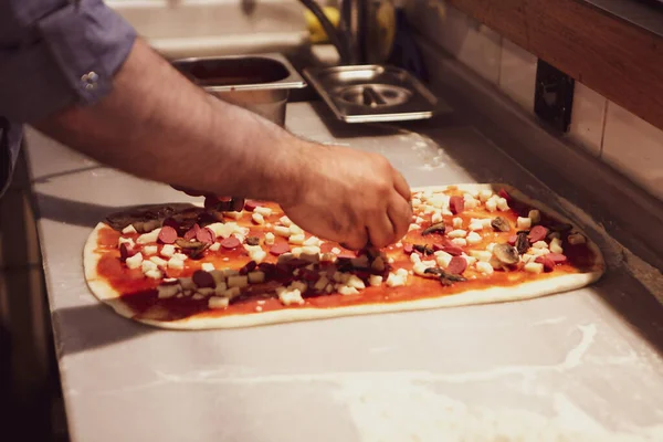 Pizza şefi ticari bir mutfakta sosu tabana koydu.