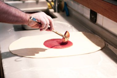 Pizza şefi ticari bir mutfakta sosu tabana koydu.