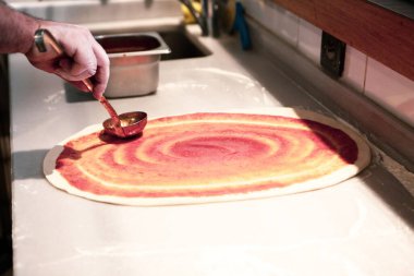 Pizza şefi ticari bir mutfakta sosu tabana koydu.