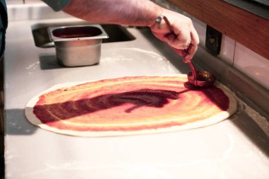 Pizza şefi ticari bir mutfakta sosu tabana koydu.