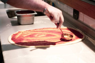 Pizza şefi ticari bir mutfakta sosu tabana koydu.