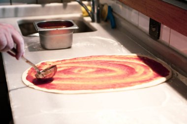 Pizza şefi ticari bir mutfakta sosu tabana koydu.