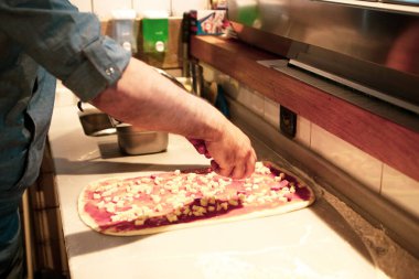 Pizza şefi ticari bir mutfakta sosu tabana koydu.