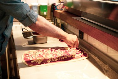 Pizza şefi ticari bir mutfakta sosu tabana koydu.