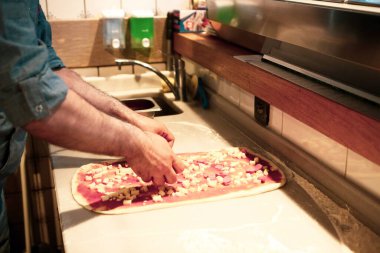 Pizza şefi ticari bir mutfakta sosu tabana koydu.