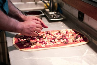 Pizza şefi ticari bir mutfakta sosu tabana koydu.