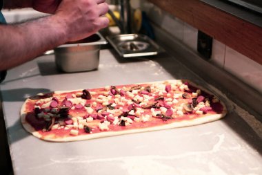 Pizza şefi ticari bir mutfakta sosu tabana koydu.