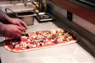 Pizza şefi ticari bir mutfakta sosu tabana koydu.