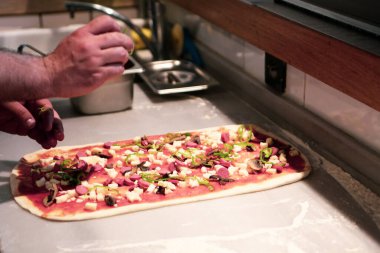 Pizza şefi ticari bir mutfakta sosu tabana koydu.