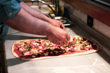 Pizza şefi ticari bir mutfakta sosu tabana koydu.