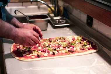 Pizza şefi ticari bir mutfakta sosu tabana koydu.