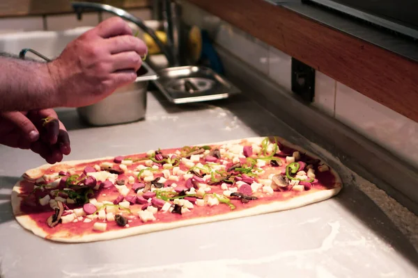 Pizza şefi ticari bir mutfakta sosu tabana koydu.