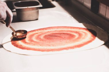Pizza şefi ticari bir mutfakta sosu tabana koydu.