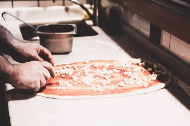 Pizza şefi ticari bir mutfakta sosu tabana koydu.
