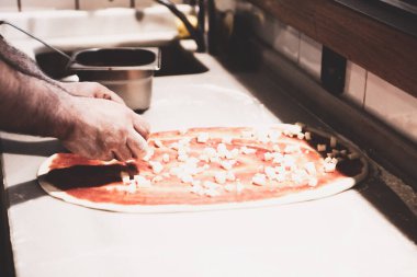 Pizza şefi ticari bir mutfakta sosu tabana koydu.