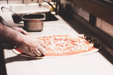 Pizza şefi ticari bir mutfakta sosu tabana koydu.