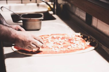 Pizza şefi ticari bir mutfakta sosu tabana koydu.