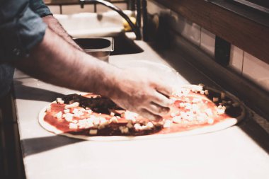 Pizza şefi ticari bir mutfakta sosu tabana koydu.