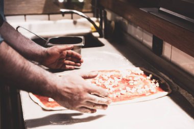Pizza şefi ticari bir mutfakta sosu tabana koydu.