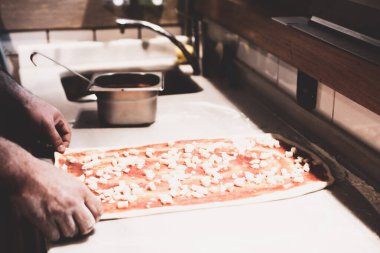 Pizza şefi ticari bir mutfakta sosu tabana koydu.