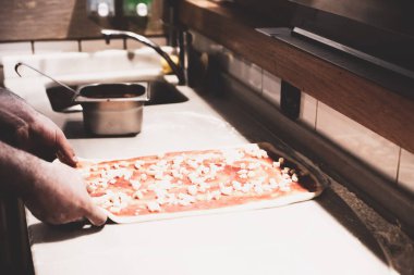 Pizza şefi ticari bir mutfakta sosu tabana koydu.