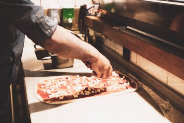 Pizza şefi ticari bir mutfakta sosu tabana koydu.