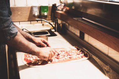 Pizza şefi ticari bir mutfakta sosu tabana koydu.