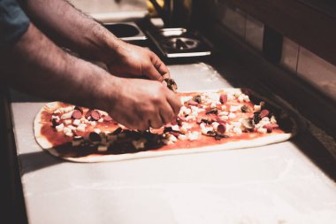 Pizza şefi ticari bir mutfakta sosu tabana koydu.