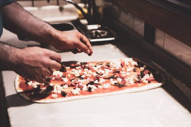 Pizza şefi ticari bir mutfakta sosu tabana koydu.
