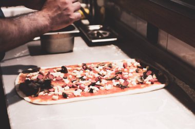 Pizza şefi ticari bir mutfakta sosu tabana koydu.