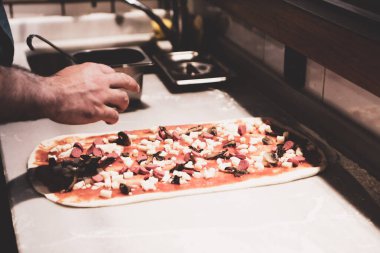 Pizza şefi ticari bir mutfakta sosu tabana koydu.