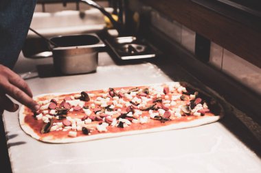 Pizza şefi ticari bir mutfakta sosu tabana koydu.