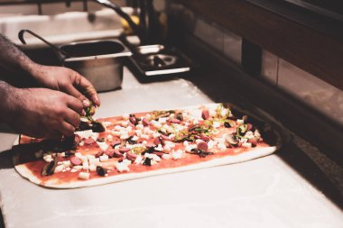 Pizza şefi ticari bir mutfakta sosu tabana koydu.