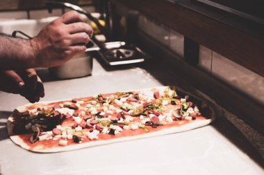 Pizza şefi ticari bir mutfakta sosu tabana koydu.