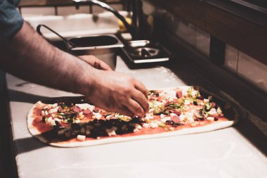 Pizza şefi ticari bir mutfakta sosu tabana koydu.