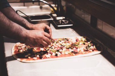Pizza şefi ticari bir mutfakta sosu tabana koydu.