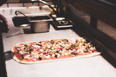 Pizza şefi ticari bir mutfakta sosu tabana koydu.