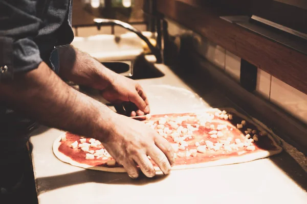 Pizza şefi ticari bir mutfakta sosu tabana koydu.