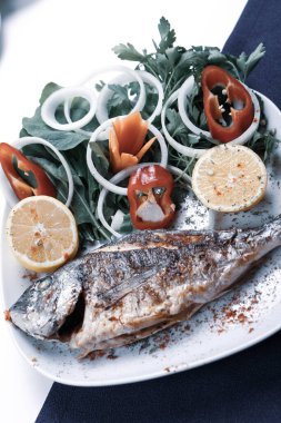 Kızarmış deniz çerezi (cupra) beyaz tabakta soğan, bahçe roketi ve limon dilimli balık.