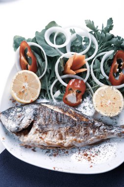 Kızarmış deniz çerezi (cupra) beyaz tabakta soğan, bahçe roketi ve limon dilimli balık.