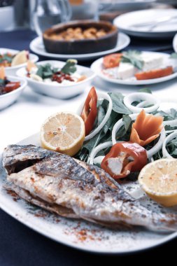 Kızarmış deniz çerezi (cupra) beyaz tabakta soğan, bahçe roketi ve limon dilimli balık.