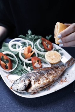 Kızarmış deniz çerezi (cupra) beyaz tabakta soğan, bahçe roketi ve limon dilimli balık.