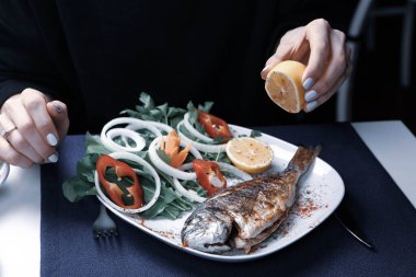 Kızarmış deniz çerezi (cupra) beyaz tabakta soğan, bahçe roketi ve limon dilimli balık.