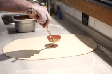 Pizza şefi ticari bir mutfakta sosu tabana koydu.