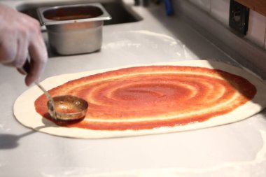 Pizza şefi ticari bir mutfakta sosu tabana koydu.