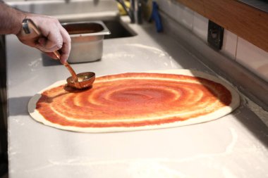 Pizza şefi ticari bir mutfakta sosu tabana koydu.