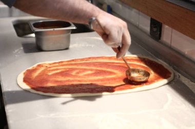 Pizza şefi ticari bir mutfakta sosu tabana koydu.