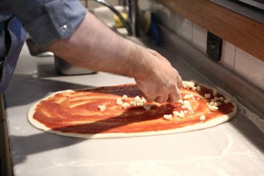 Pizza şefi ticari bir mutfakta sosu tabana koydu.