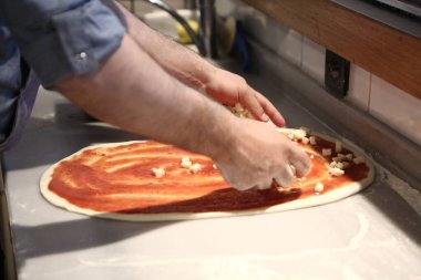 Pizza şefi ticari bir mutfakta sosu tabana koydu.